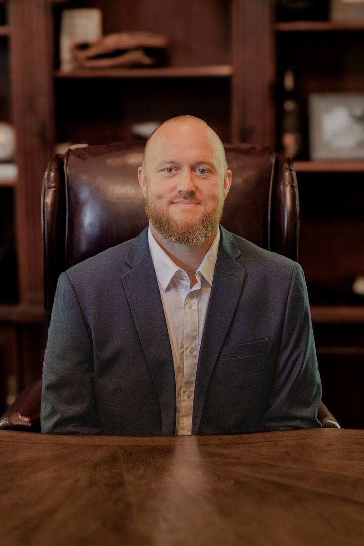 Daniel Reed II, seated at a wooden desk in a jacket and open-collared shirt